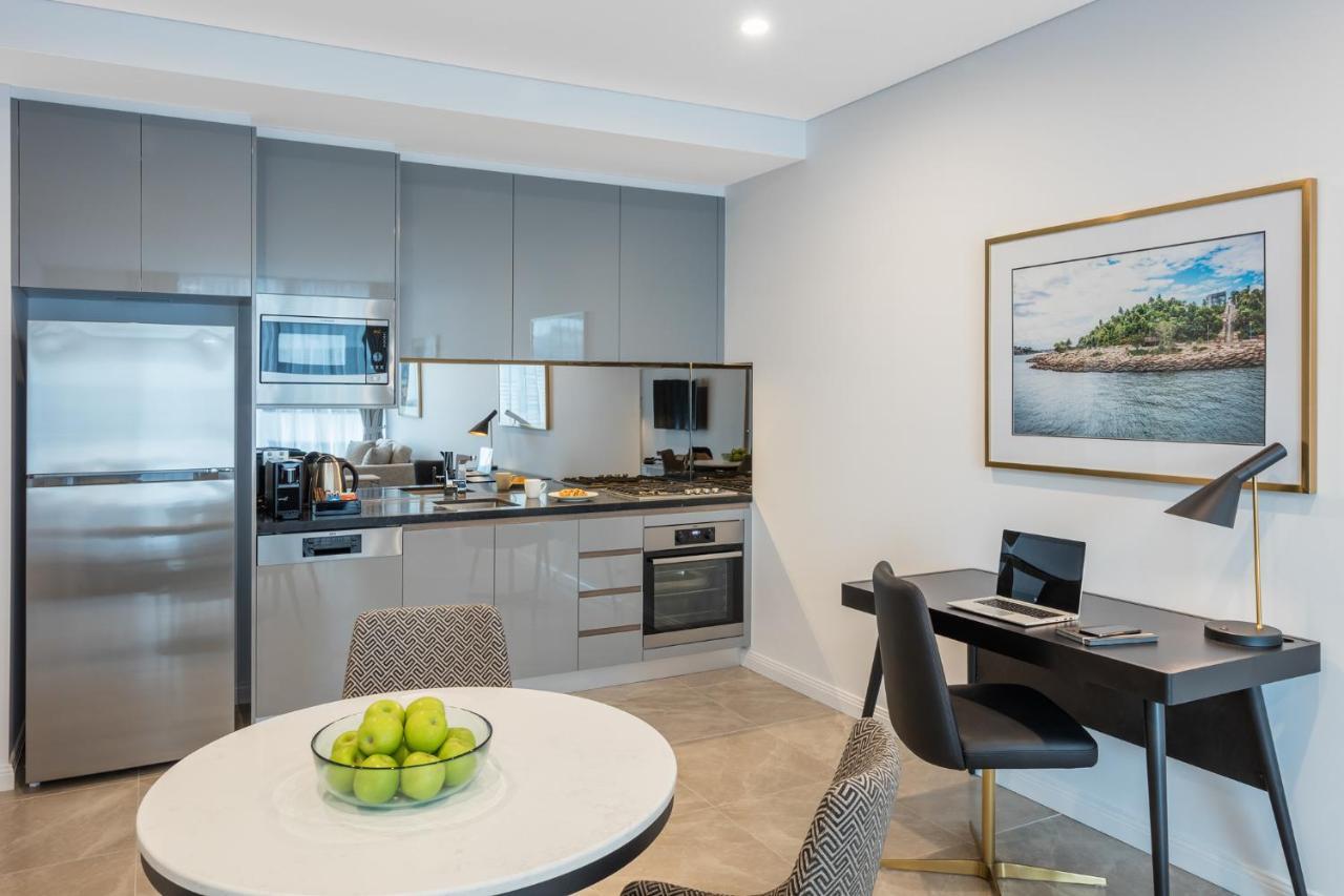 Meriton Suites Sussex Street, Σίδνεϊ Εξωτερικό φωτογραφία The photo shows a modern kitchen and dining area in an apartment. The kitchen features sleek gray cabinetry, a stainless steel fridge, and a microwave. There is a countertop with cooking appliances, including an oven and stovetop. A small round dinin