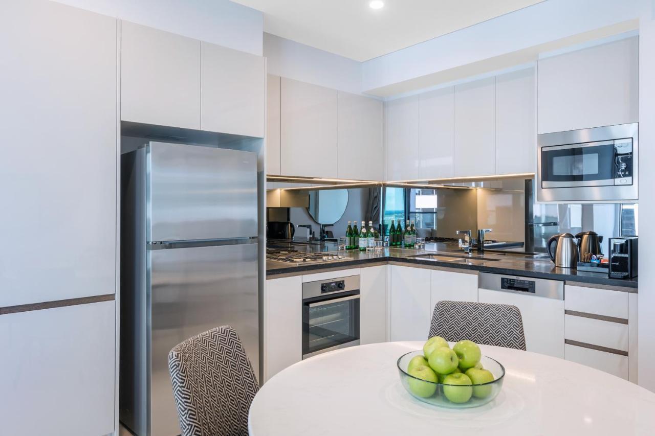 Meriton Suites Sussex Street, Σίδνεϊ Εξωτερικό φωτογραφία The photo displays a modern kitchen with a sleek design. It features light-colored cabinetry and a countertop with a polished finish. On the left, there is a stainless steel refrigerator. The kitchen is equipped with various appliances, including an 