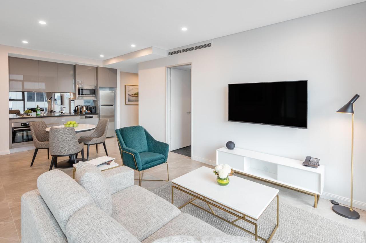 Meriton Suites Sussex Street, Σίδνεϊ Εξωτερικό φωτογραφία The photo shows a modern living room area. It features a light gray sofa and a coffee table with a decorative plant. There are two chairs, one in teal and a round one, positioned around the coffee table. A flat-screen TV is mounted on the wall, and t