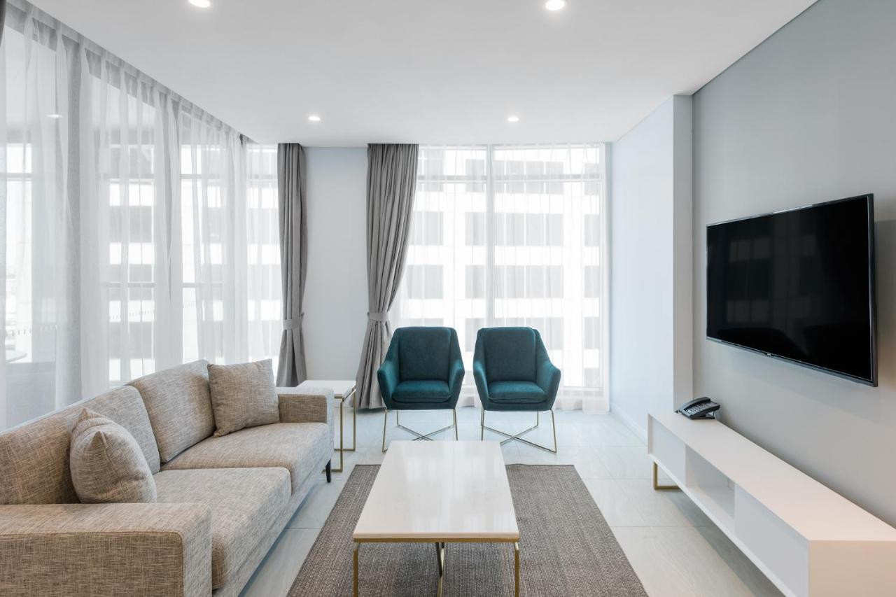Meriton Suites Sussex Street, Σίδνεϊ Εξωτερικό φωτογραφία The photo shows a modern living room equipped with a light gray sofa, two teal chairs, and a coffee table in the center. The room features large windows with sheer curtains, allowing natural light to illuminate the space. There is a white media conso