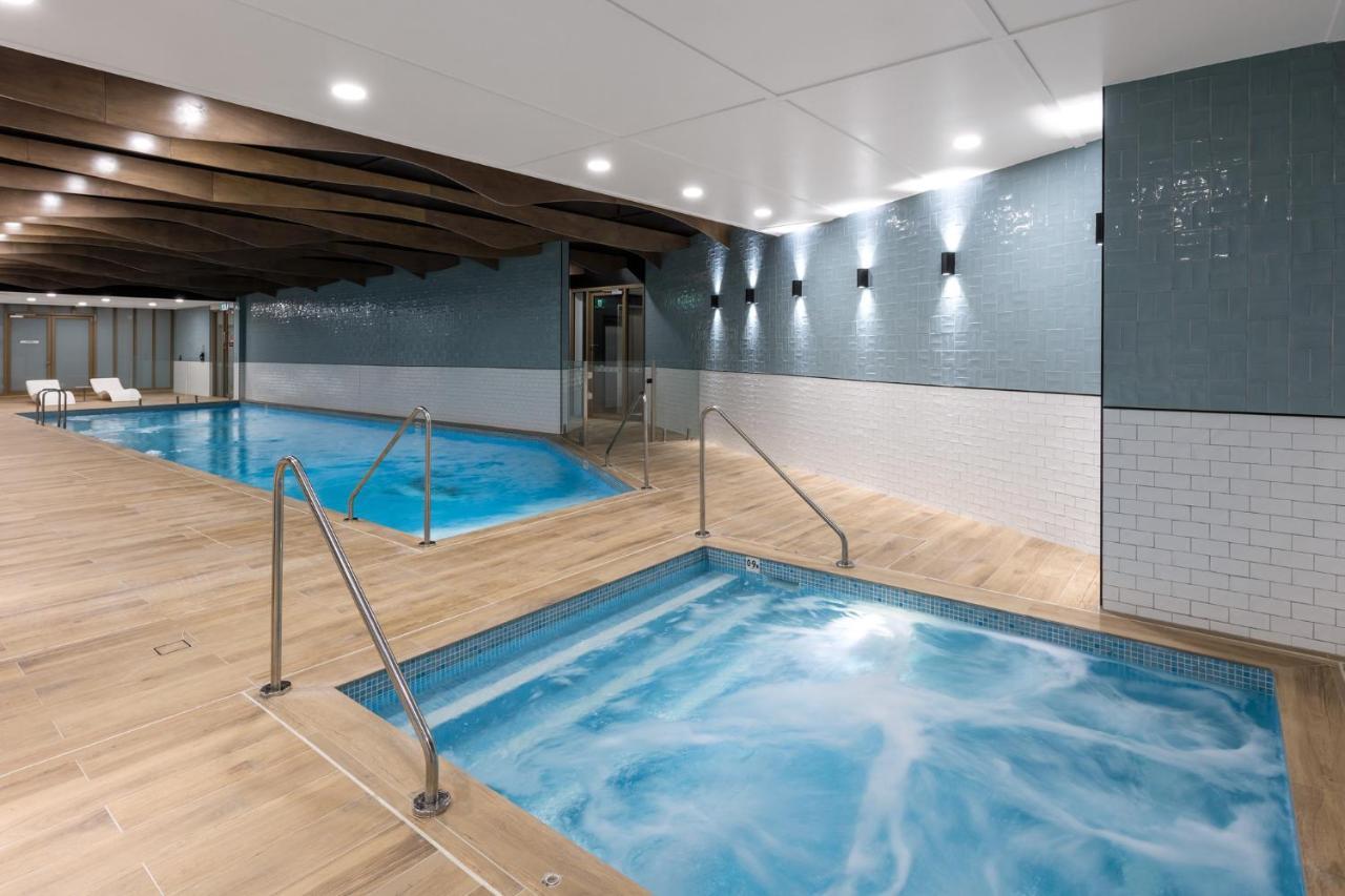 Meriton Suites Sussex Street, Σίδνεϊ Εξωτερικό φωτογραφία The photo shows a modern indoor spa area. There are two pools: one is larger and has a clear blue water, while the other is smaller, possibly a hot tub, with jets creating bubbles. The walls are a mix of blue tiles and white tiles, and the floor is m