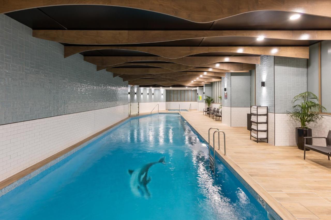 Meriton Suites Sussex Street, Σίδνεϊ Εξωτερικό φωτογραφία The photo shows an indoor swimming pool. The pool features clear blue water, and there is a dolphin swimming in it. The surrounding area has a modern design with curved wooden beams on the ceiling, and the walls are tiled in light colors. There are a