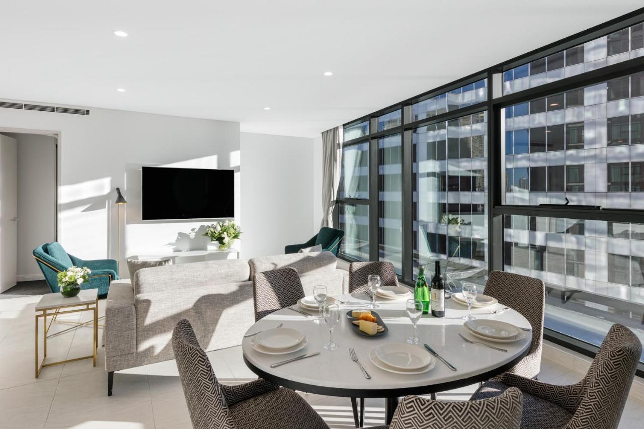 Meriton Suites Sussex Street, Σίδνεϊ Εξωτερικό φωτογραφία The photo shows a modern and stylish living room and dining area. In the foreground, there is a round dining table set for a meal with plates, cutlery, and drinks. The seating arrangement includes comfortable chairs around the table. 

In the backgro