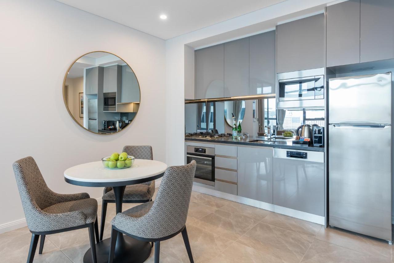 Meriton Suites Sussex Street, Σίδνεϊ Εξωτερικό φωτογραφία The photo features a modern kitchen and dining area. The kitchen has sleek grey cabinets and countertops, with built-in appliances including an oven and possibly a cooktop. There's a large stainless steel refrigerator on the right. A round dining tab