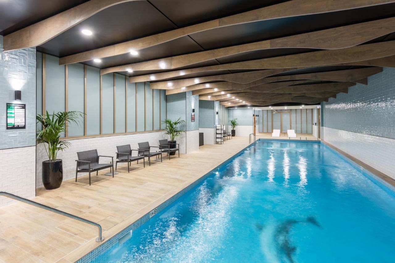 Meriton Suites Sussex Street, Σίδνεϊ Εξωτερικό φωτογραφία The photo shows an indoor swimming pool area. The pool has clear blue water and is flanked by a wooden deck. There are several lounge chairs arranged along one side of the pool. The ceiling features a modern design with wooden beams and recessed ligh
