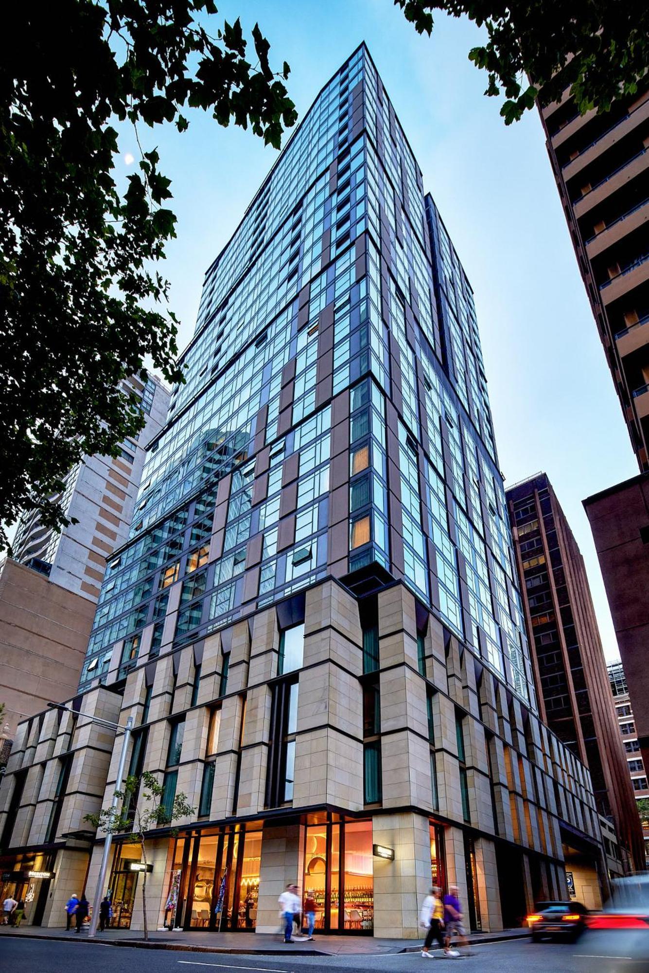 Meriton Suites Sussex Street, Σίδνεϊ Εξωτερικό φωτογραφία The photo shows a modern high-rise building with a sleek, glass facade reflecting its surroundings. The structure features a combination of glass and concrete materials, with multiple stories visible. The lower part of the building has a sturdy, text