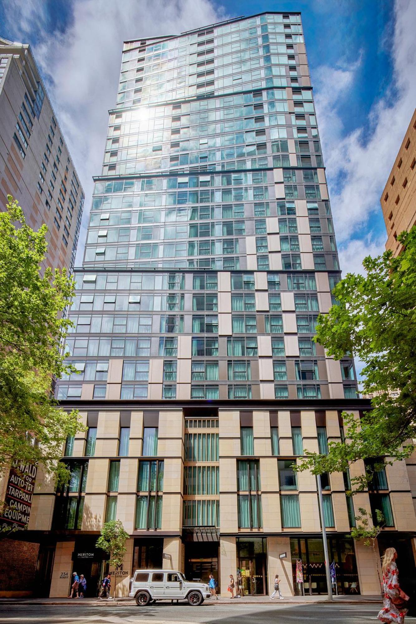 Meriton Suites Sussex Street, Σίδνεϊ Εξωτερικό φωτογραφία The photo shows a tall modern building with a glass facade and various architectural design elements. The structure has multiple stories, with large windows that reflect the surrounding environment. At the base, there are sections that appear to have